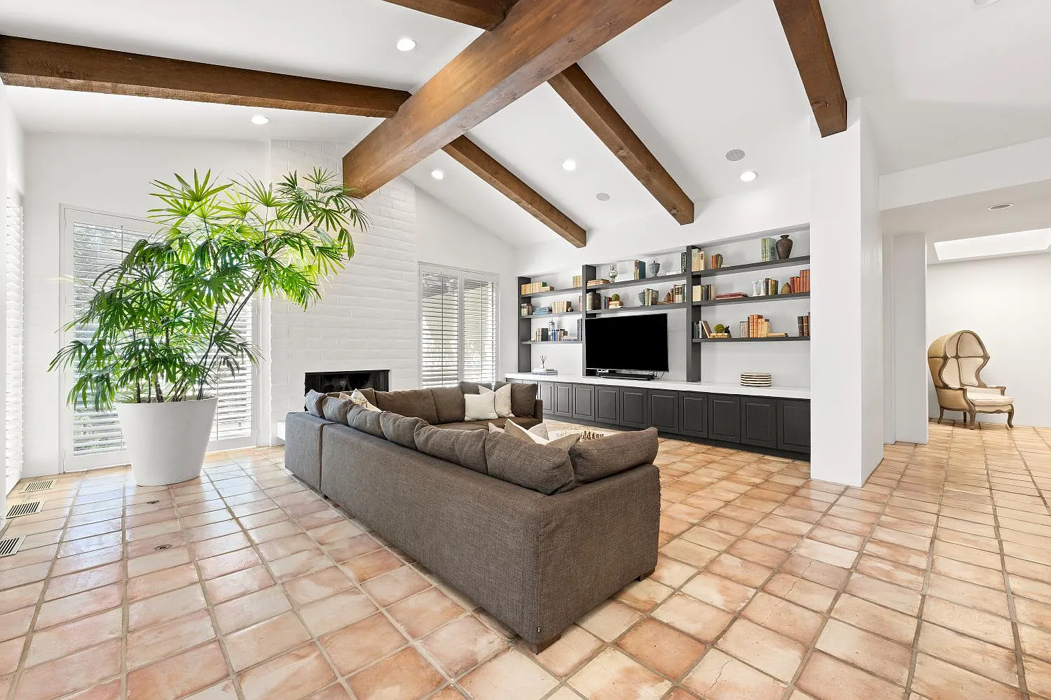 The media area has a white brick fireplace and a large sectional facing a built-in wall of cabinetry and open shelving framing a TV in the center.