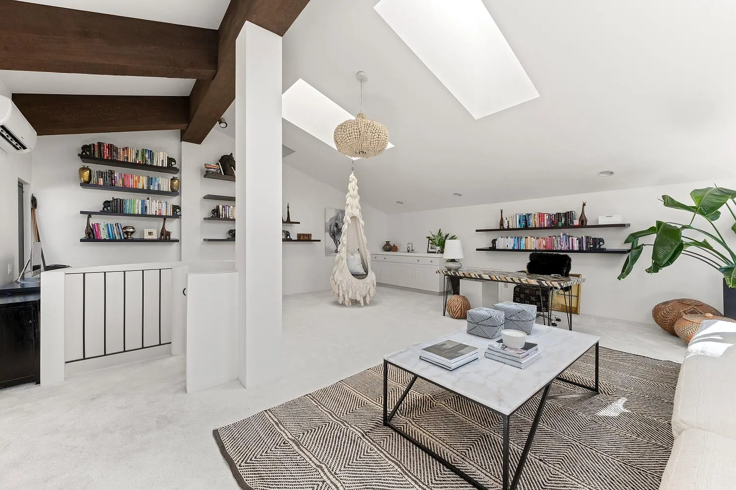 Built-in cabinetry and floating shelves line the walls beneath a vaulted ceiling with skylights and exposed wood beams.
