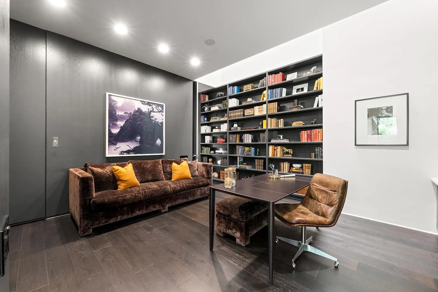 The second office is more enclosed and formal, with dark wood flooring, a full wall of built-in bookshelves, and a deep-toned accent wall.