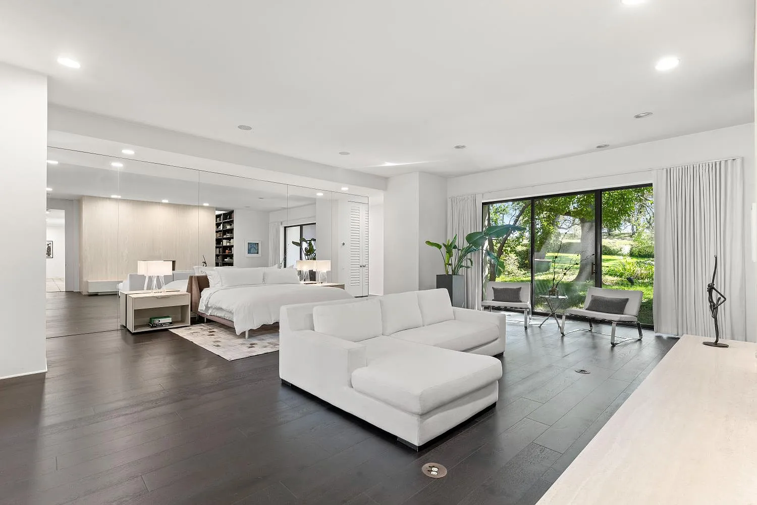 Inside the bedroom, the bed sits against a mirrored wall on one end of the room across from a large lounge area positioned directly in front of it.