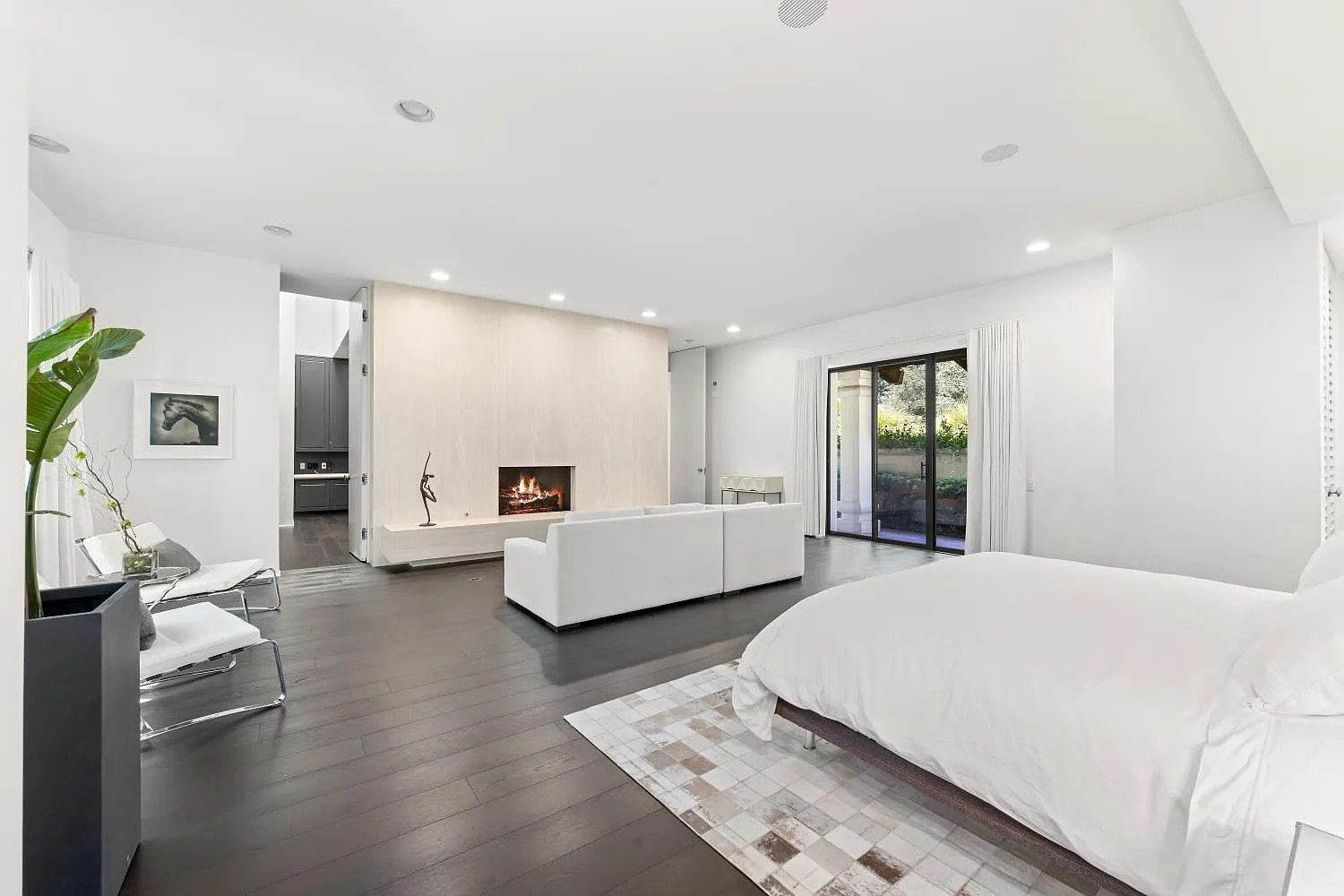 Primary suite bedroom with a bed across from L-shaped sofa faces a large fireplace wall.