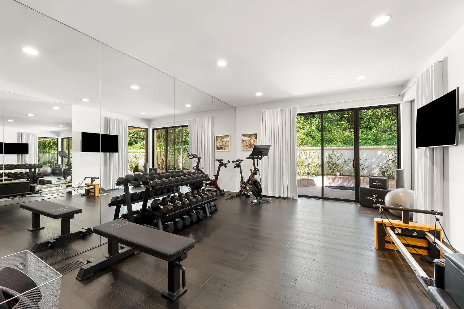 Home gym with mirrored walls lining one side of the room, while free weights, cardio equipment, and a Pilates machine fill out the space.