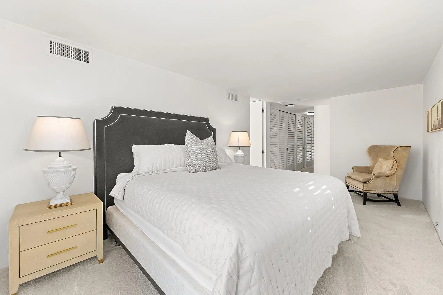 The room is furnished simply with a bed framed by matching nightstands and a reading chair placed in the corner.