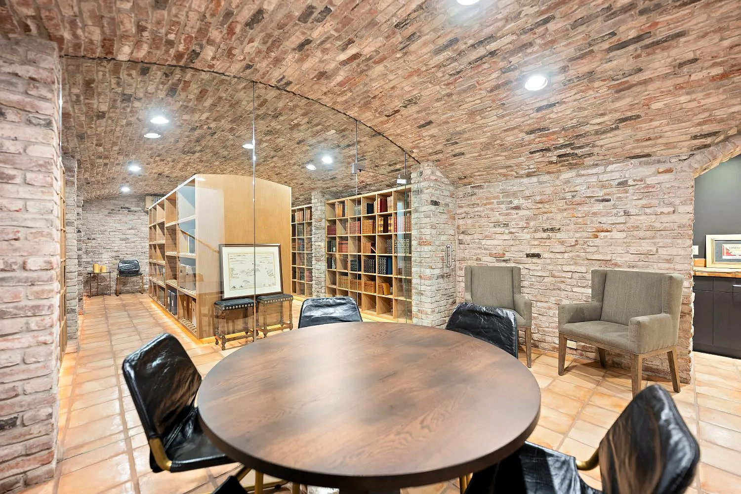 A round table and surrounding chairs create a small tasting or reading area, with glass panels separating the seating space from the cellar.