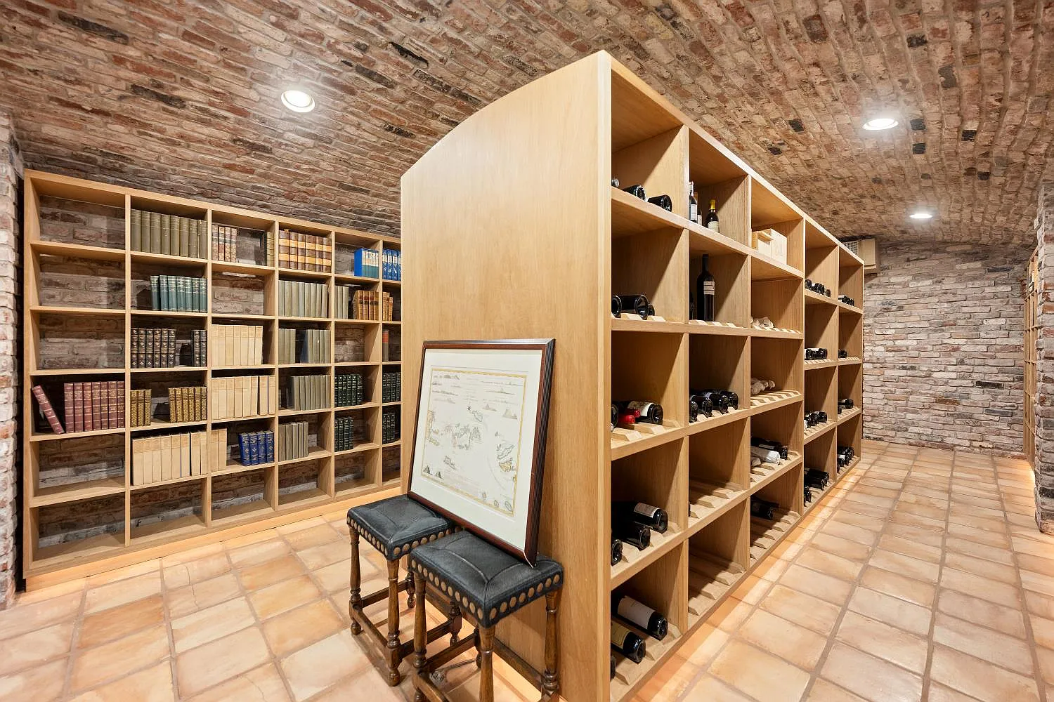 Individual cubbies hold bottles along the center shelves, while floor-to-ceiling bookcases line the outer brick walls.