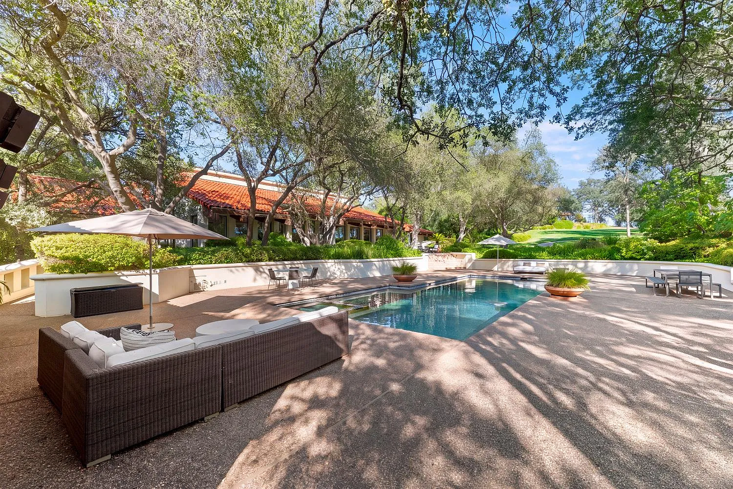 The swimming pool is surrounded by a paved deck with multiple seating areas, umbrellas, and space for lounging along the water.