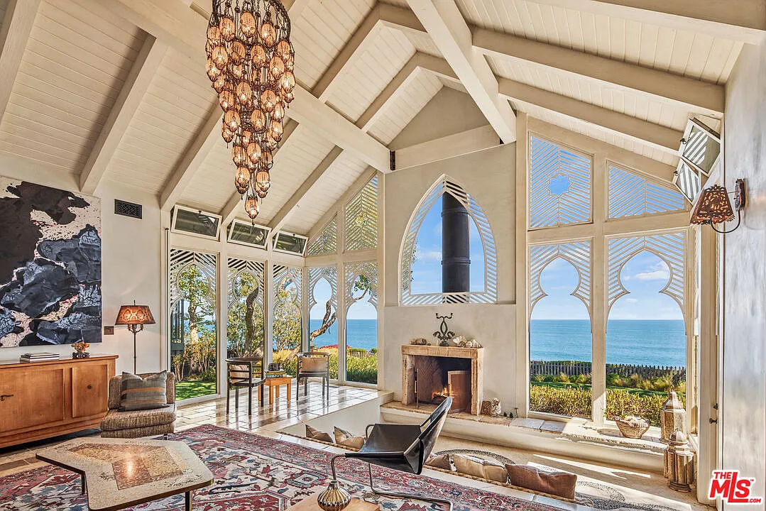 A sunken lounge faces a fireplace surrounded by tall geometric windows that frame blue-water views.