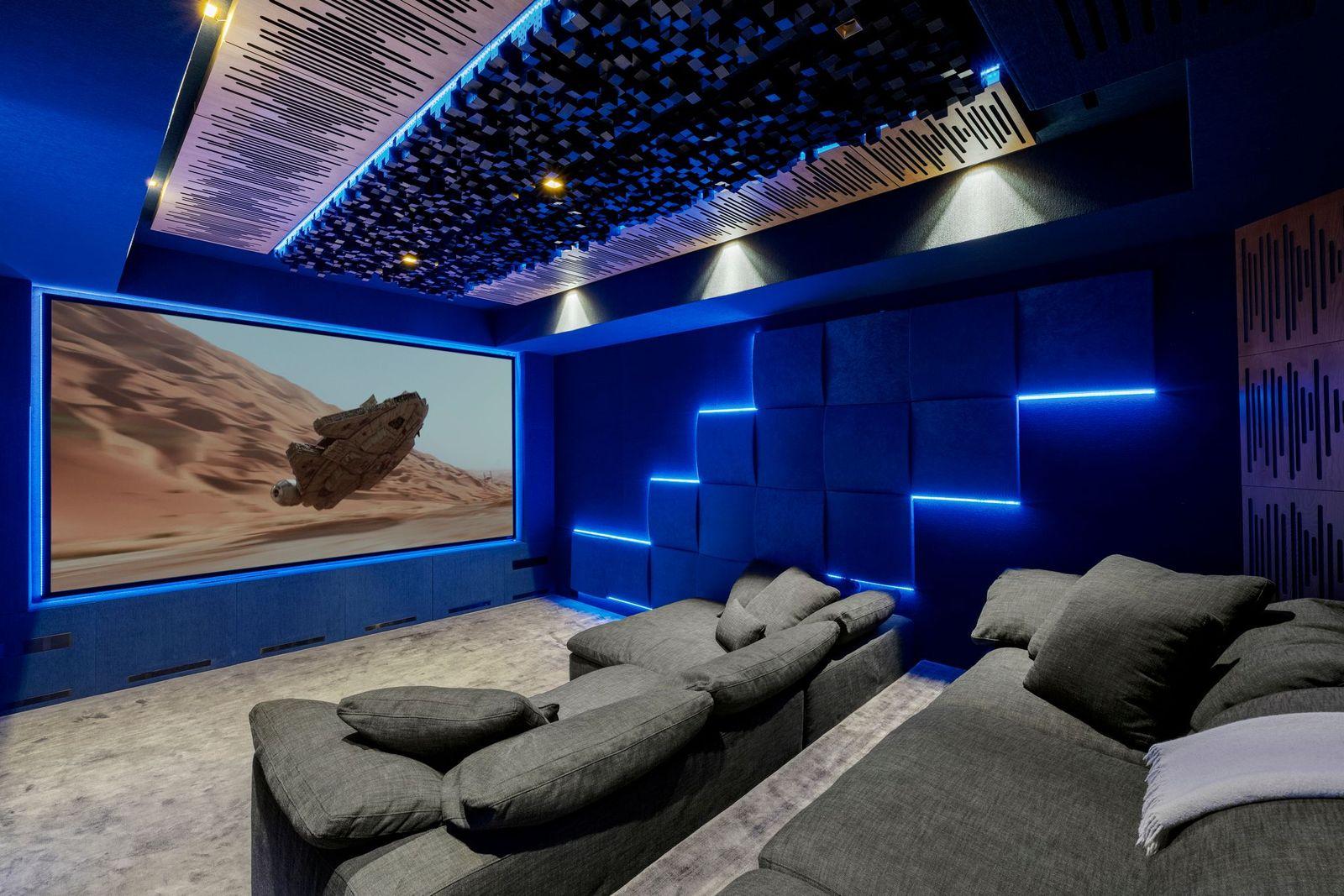 The soundproof theater is finished in deep blue, with tiered gray seating facing a wall-sized screen powered by a 4K laser projector. 