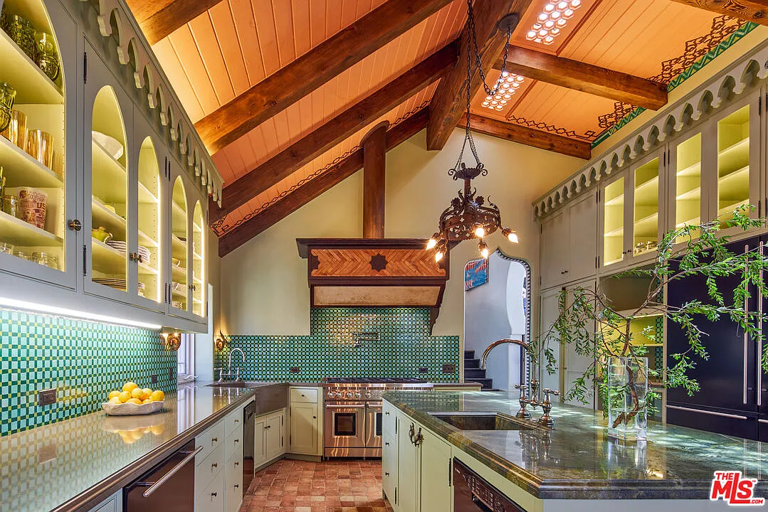 Arched glass-front cupboards, a green mosaic backsplash, and a large central island give the space much of its visual character.