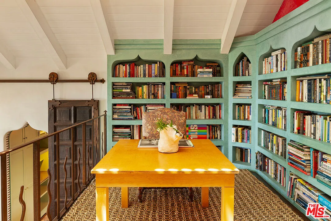Turquoise built-in bookshelves wrap the upper level beneath the pitched ceiling, while a wood table creates a place to read or work.
