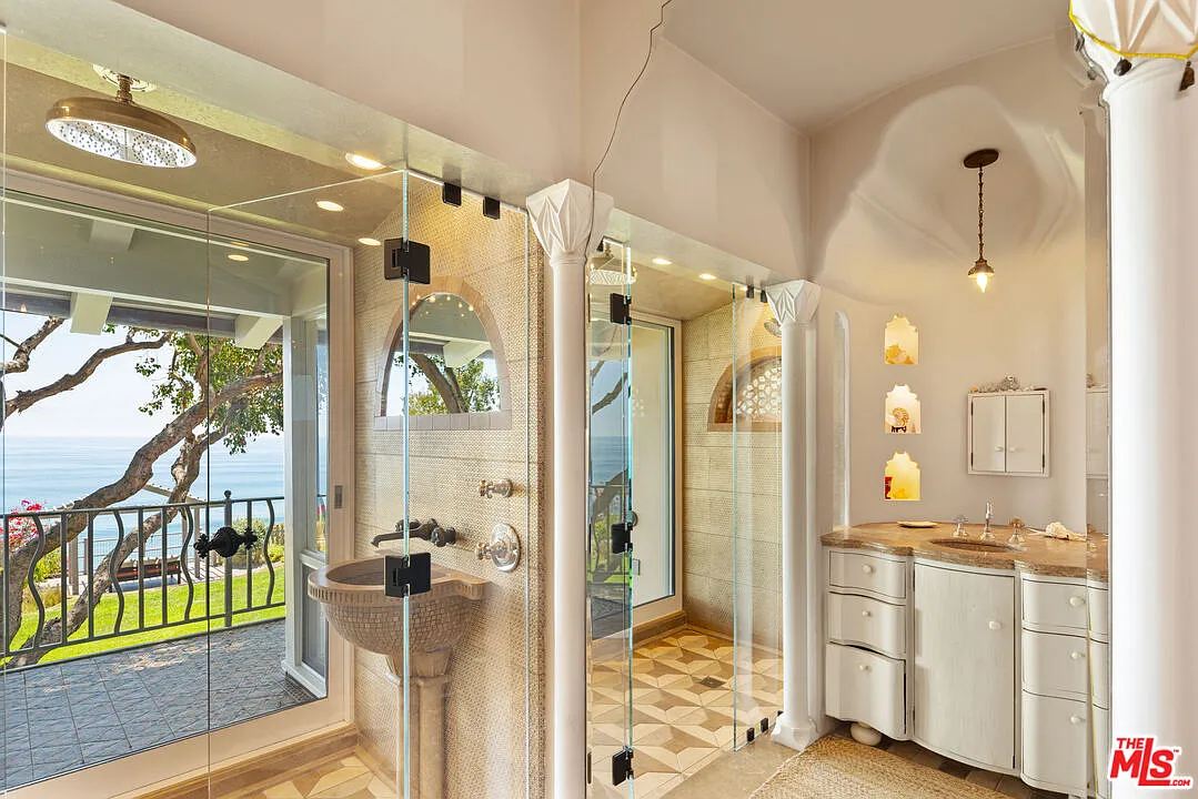 The bathroom has two separate glass-enclosed showers placed between opposite vanities.
