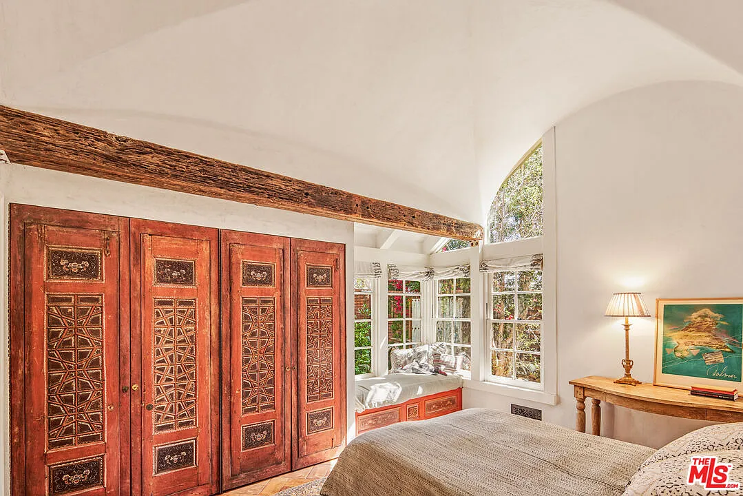 The bed faces a wall of carved wood closet doors and a built-in window seat tucked into the far corner beneath windows and a curved ceiling.