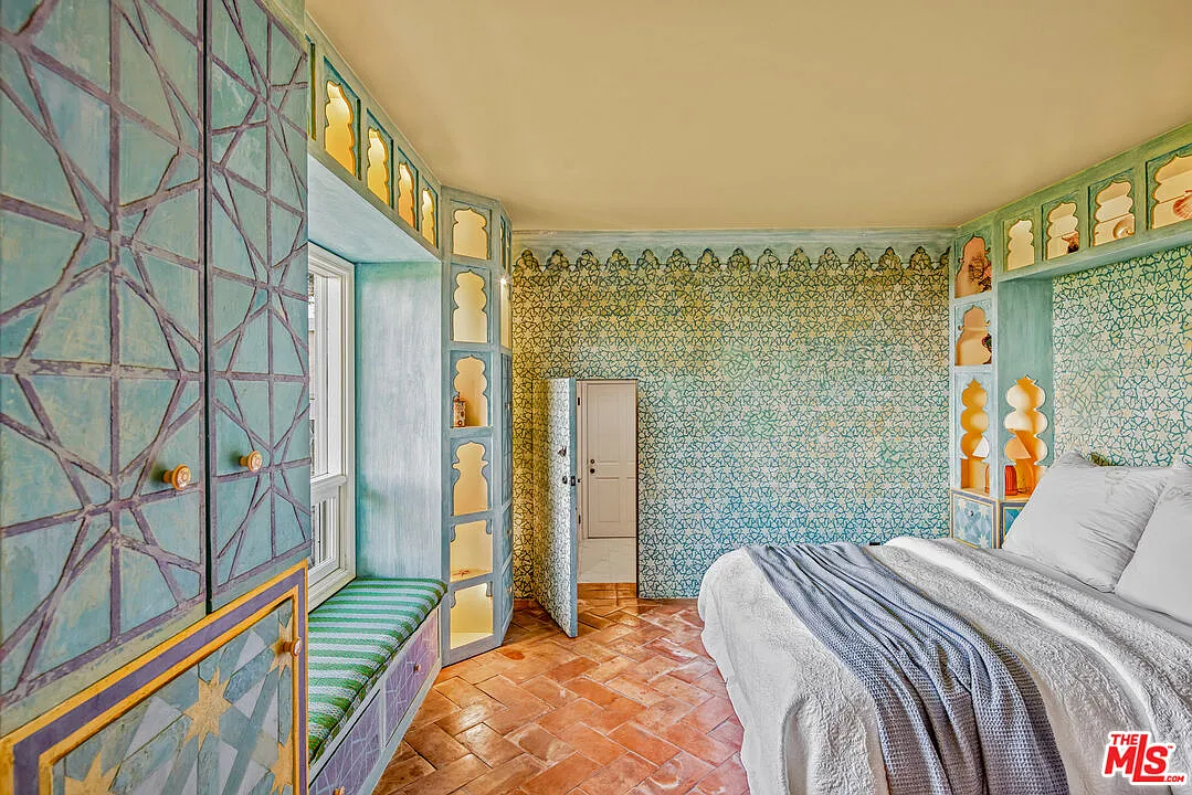 Bedroom with turquoise walls covered in intricate painted patterns and built-in niches wrapping around the bed and window seat.