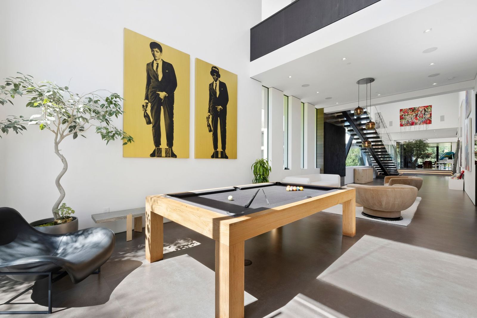 A sitting area with curved chairs and a white sofa occupies one end, while a pool table stands beneath the open upper level.