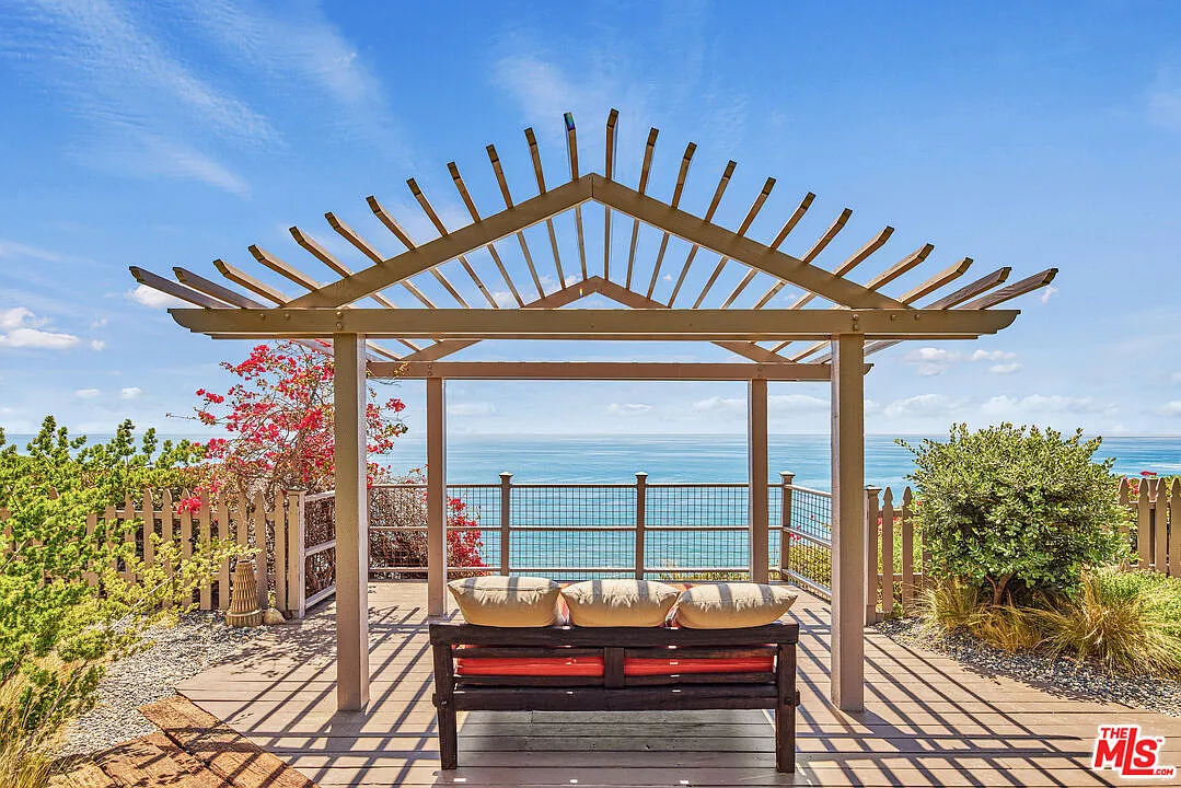 Closer to the edge of the property, a bench is placed beneath a wood pergola sitting above the bluff with an unobstructed view across the Pacific.