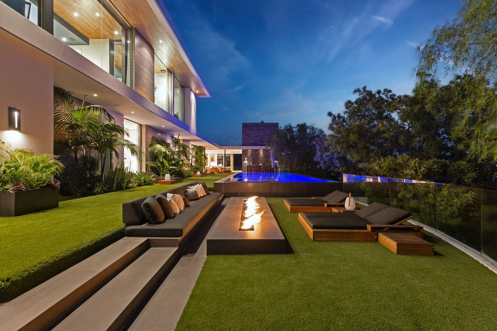 A few steps below, the opposite end of the yard drops into a sunken lounge built around a long linear fire feature.