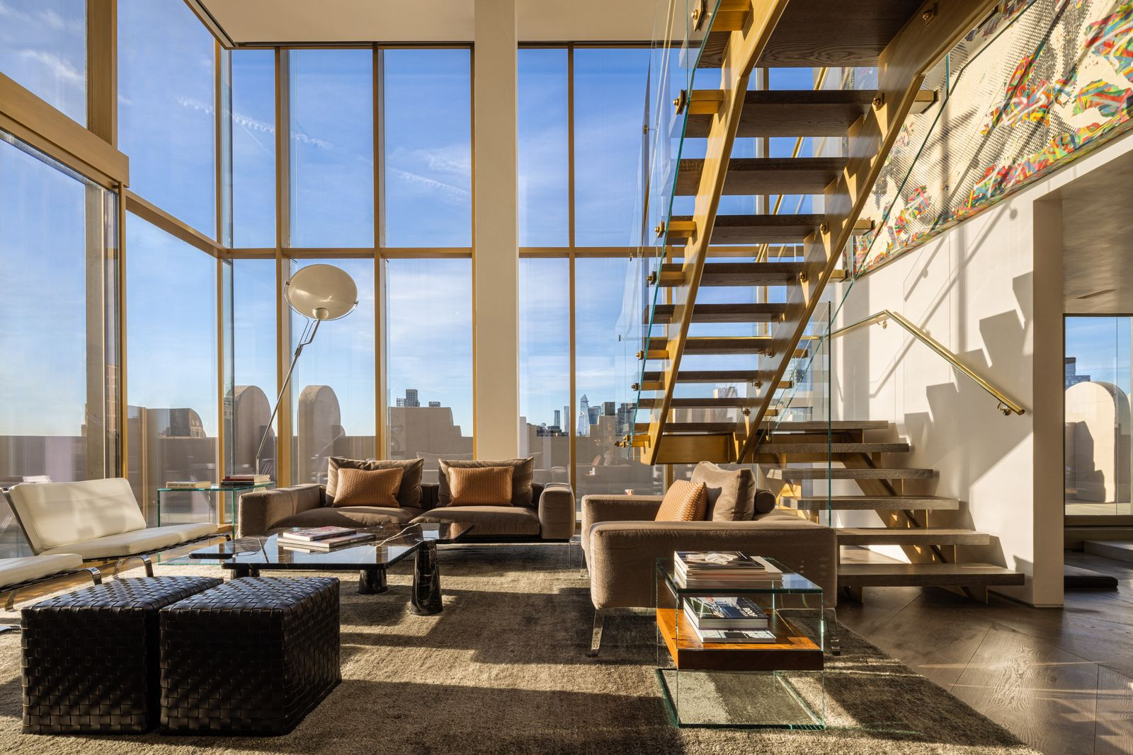 A double-height library and media room bathed in sunlight is next to a sculptural steel staircase with Starphire glass railings.