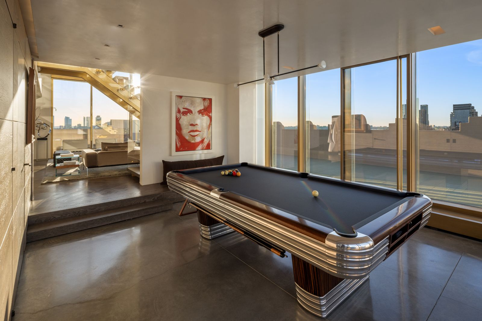 A game room with a billiards table, positioned along a wall of floor-to-ceiling windows overlooking the city.