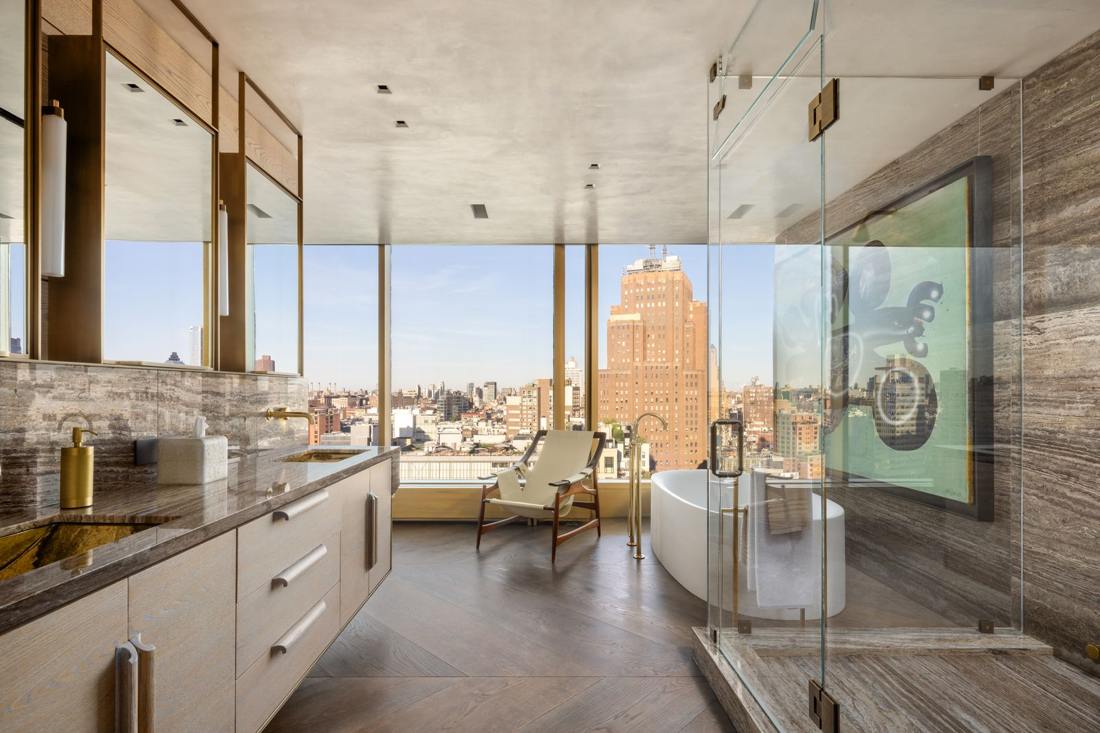 Along one side, the floating vanity stretches beneath mirrors framed by slim brass supports and on the other is a glass-enclosed steam shower.