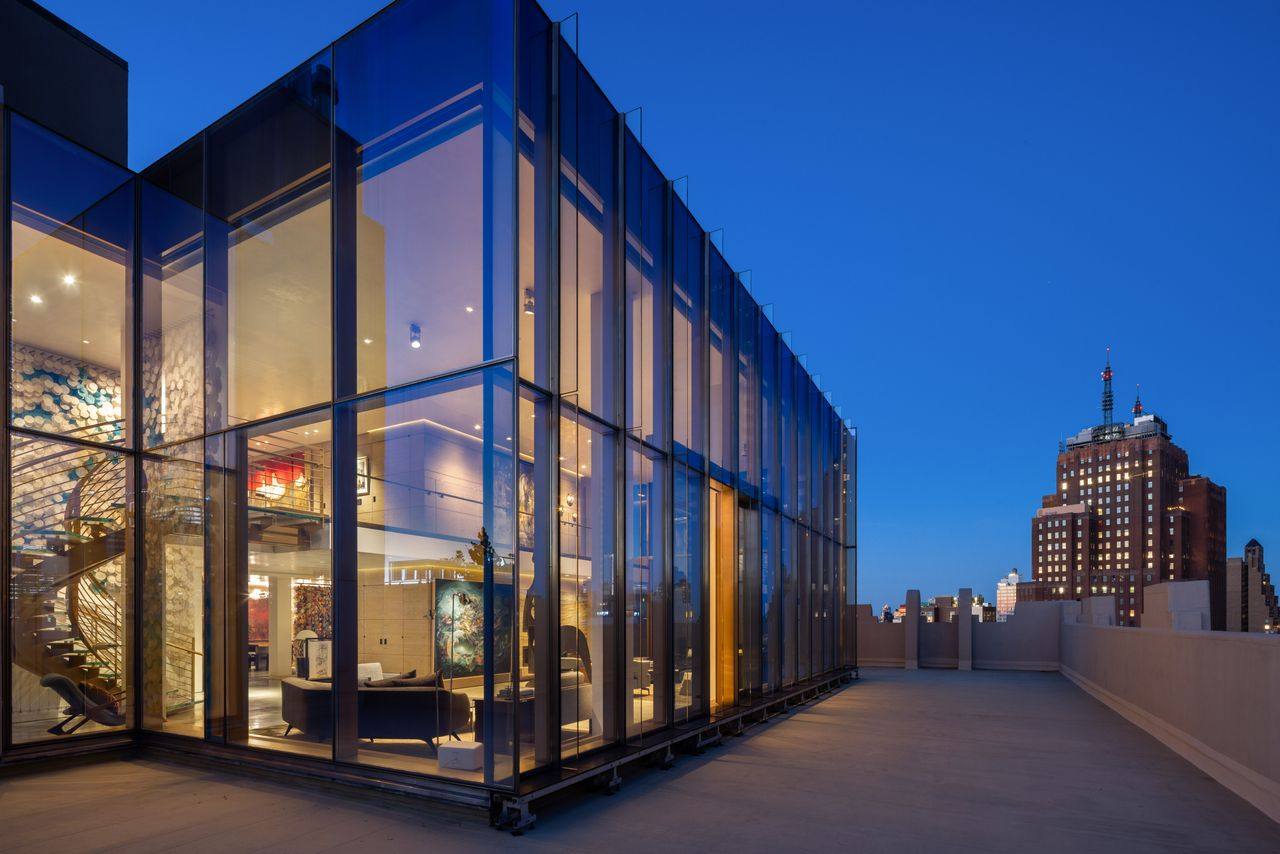 Long stretches of paving run beside the double-height living spaces, where floor-to-ceiling windows keep the interiors visually connected to the skyline.
