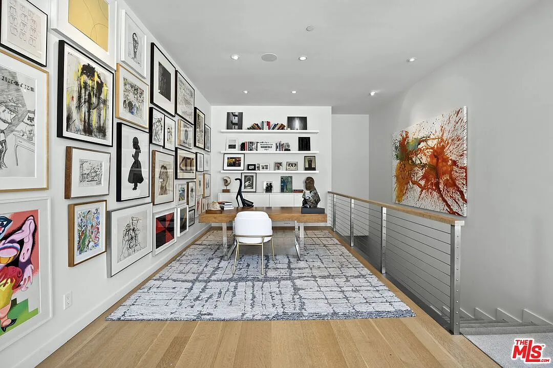 A wood desk sits at the center of a patterned rug, with floating shelves and low cabinetry forming a clean backdrop for books, photographs, and sculpture.