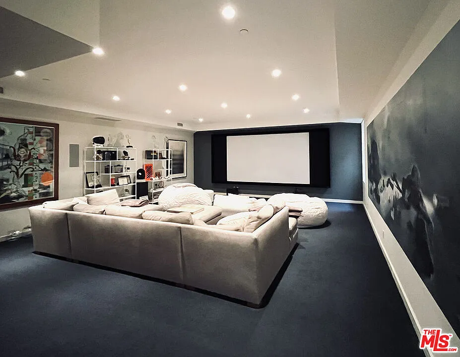 Down the stairs, the lower level opens into a media room arranged around a large projection screen set into a dark feature wall.