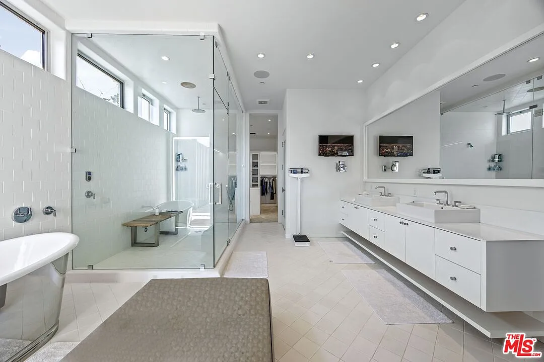 Bright en-suite bathroom, where two floating vanities run beneath one long wall mirror across from a large glass-enclosed shower and a freestanding metal soaking tub.