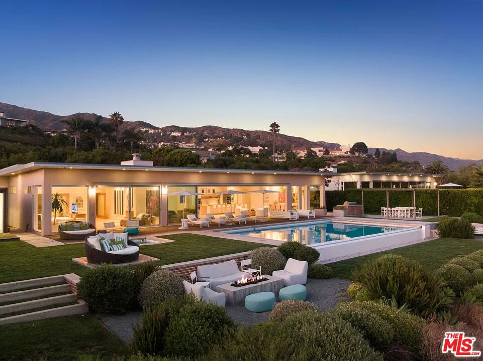 Stepping through the glass doors, the great room and primary suite continues onto a long wood deck that runs beside the house and the infinity-edge pool.