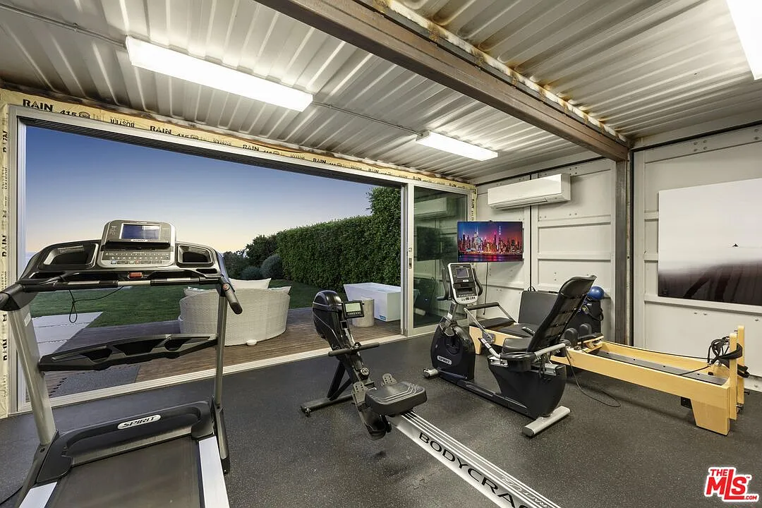 Off one side of the lawn, a separate exercise pavilion opens through sliding glass doors and contains cardio equipment, weights, and a pilates machine.