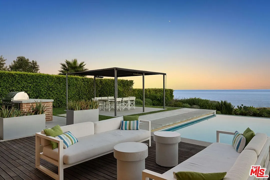 Across the lawn, an outdoor kitchen is built into a brick-and-stone counter beside a covered dining cabana.