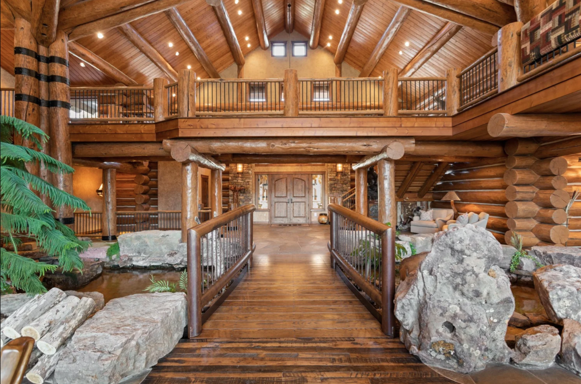A wood bridge connects the entrance to the great room, passing over a flowing trout stream that winds between boulders.