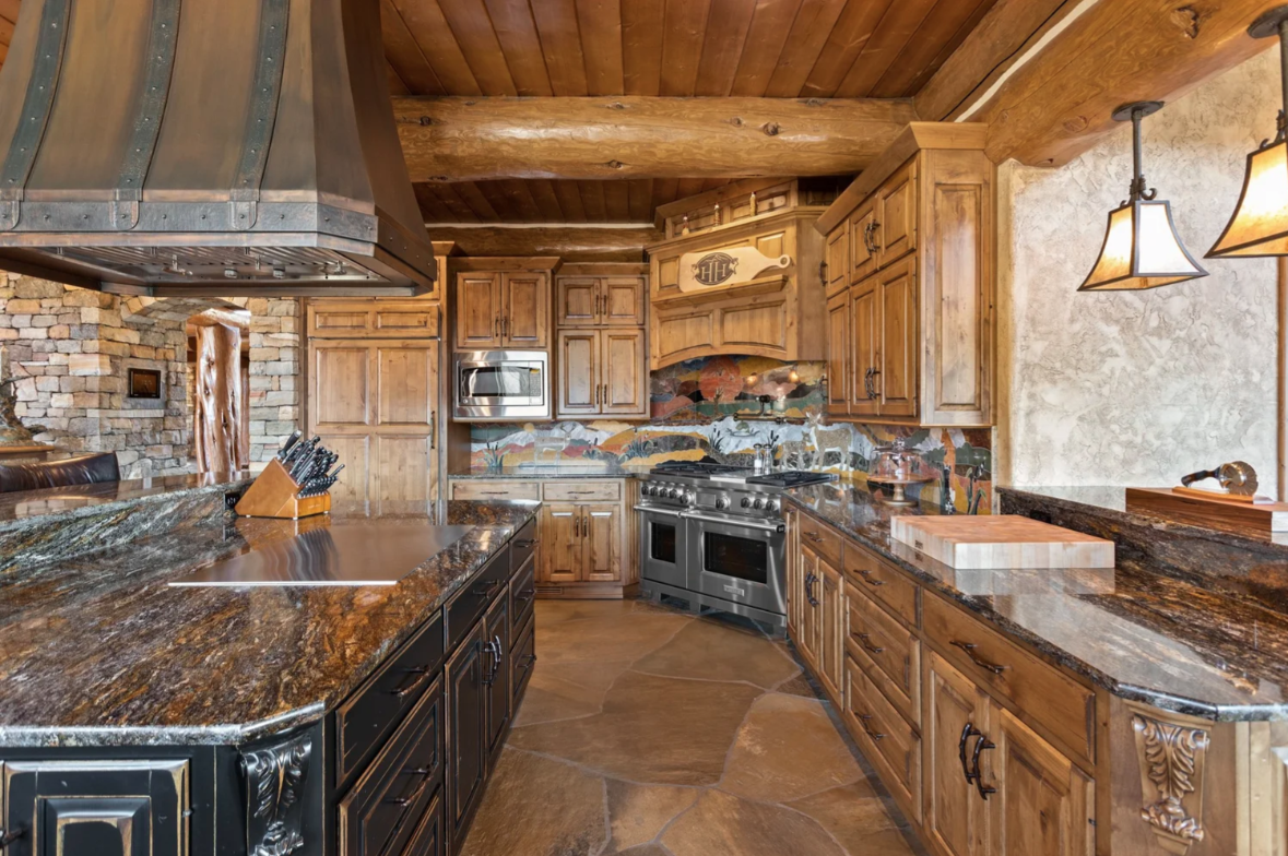 Within the island is a built-in hibachi grill that sits beneath an oversized commercial-grade exhaust hood, while a large range with double ovens sits in the corner of the room.