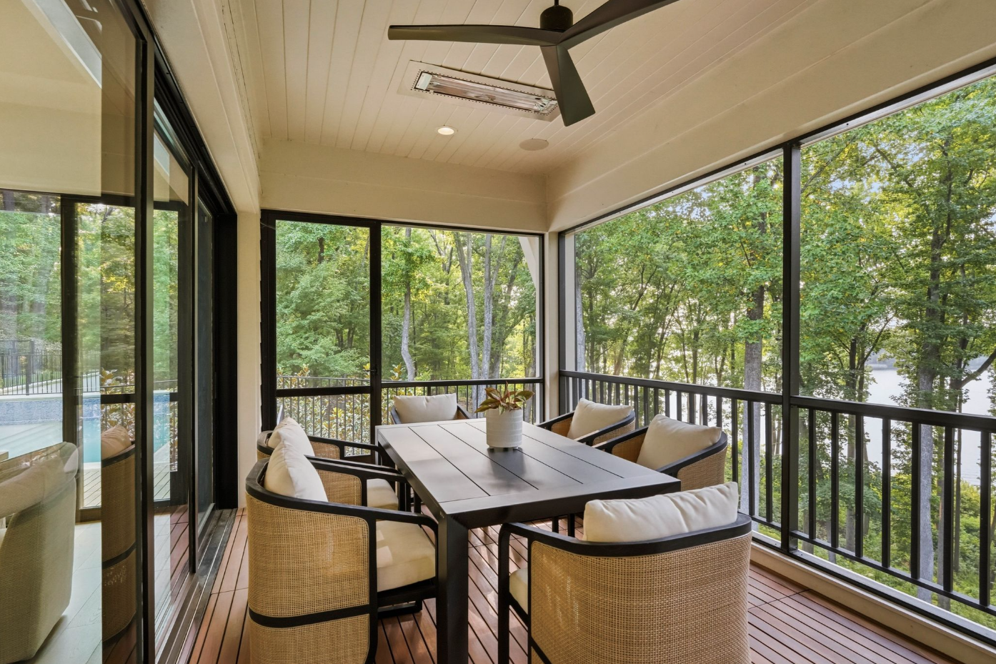 One end is arranged for outdoor dining, with a rectangular table placed beside screened openings that preserve lake views through the trees.
