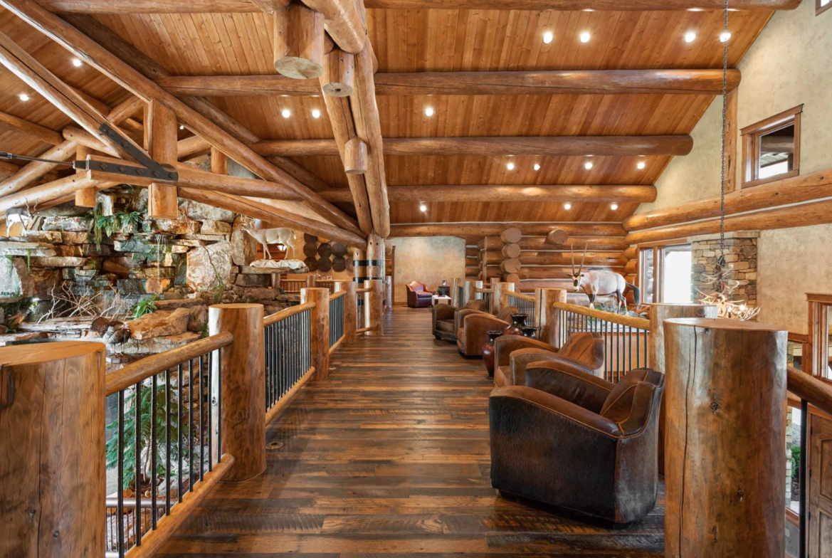 Leather chairs are spaced along the walkway between thick log posts, with the railing opening views down toward the waterfall and main living space.