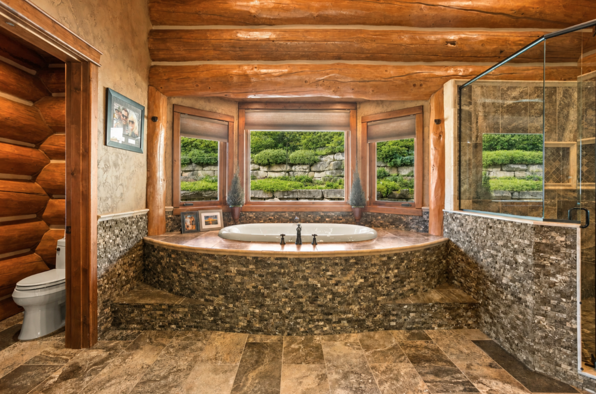 Between the shower and toilet, a soaking tub is built into a raised stone surround beneath three windows overlooking the landscaped grounds.
