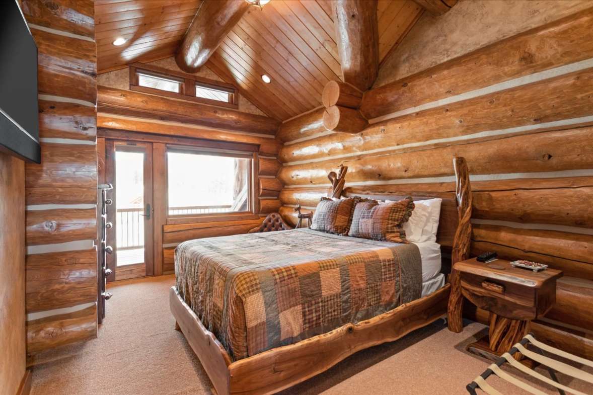 The next bedroom is more compact and enclosed, with rounded log walls wrapping a rustic wood bed and a nearby glass door that opens directly to a private balcony.