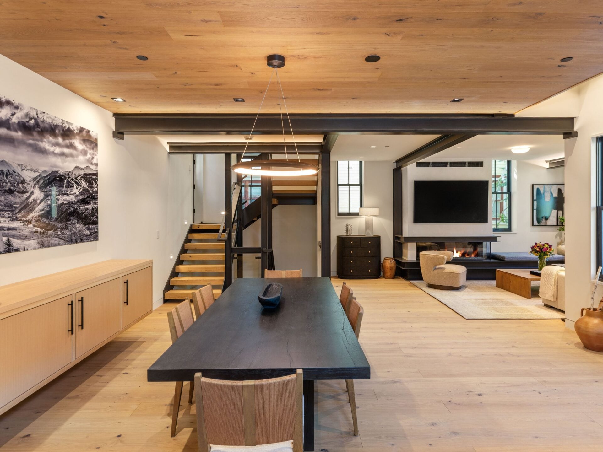 A long dining table runs through the center of the room beneath a circular pendant, with built-in cabinetry lining one wall for additional storage.