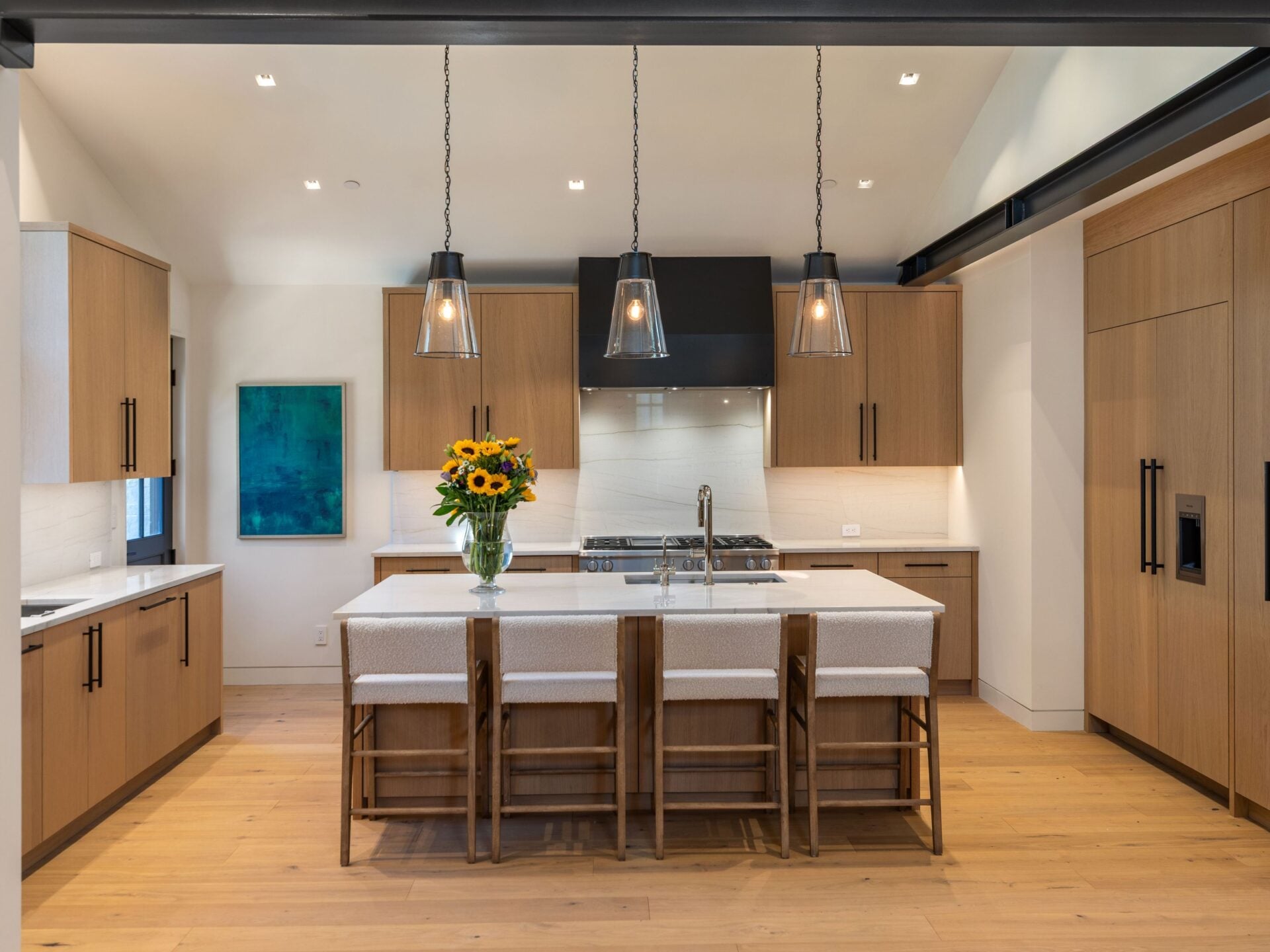 Light wood cabinetry continues around the room, incorporating a paneled refrigerator, additional storage, and a professional-style range set beneath a wide black hood.
