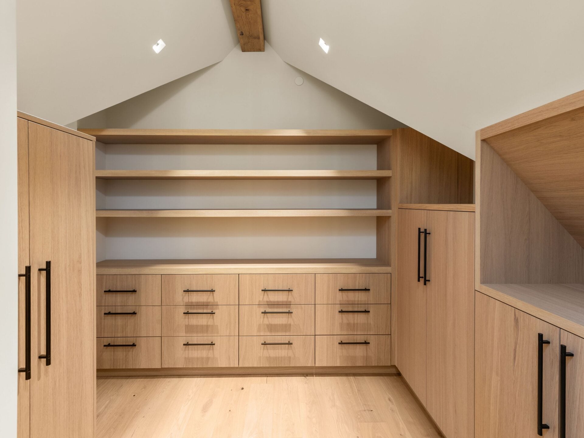 A walk-in closet with custom wood cabinetry, open shelving, deep drawers, and full-height storage built into the angles of the roofline.