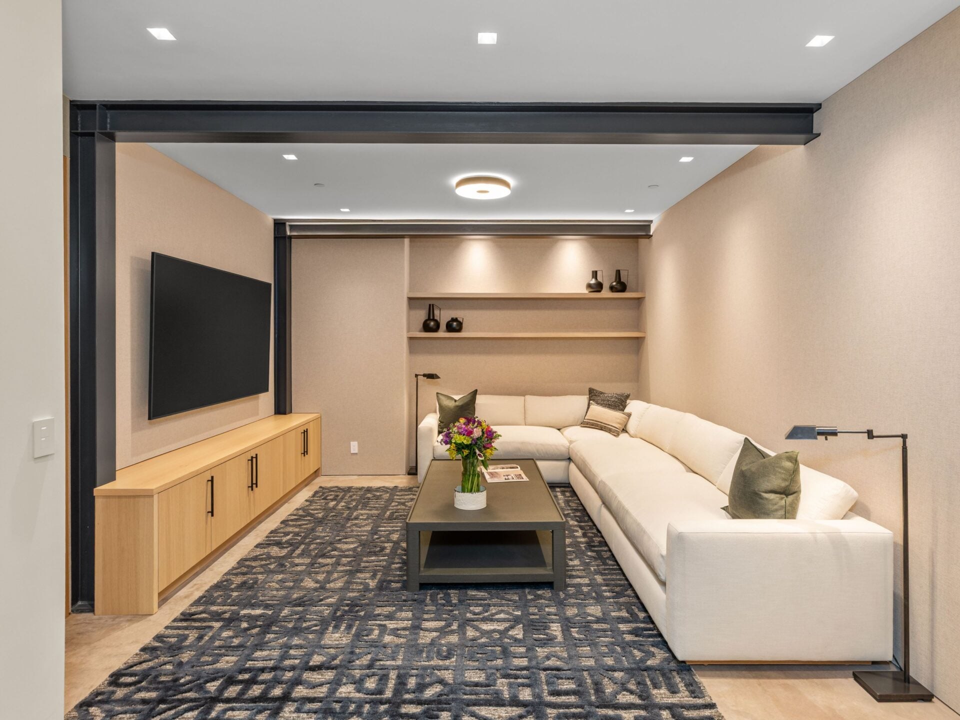 A dedicated media and entertainment room features a large sectional facing a wall-mounted television and a low built-in console running beneath it. 