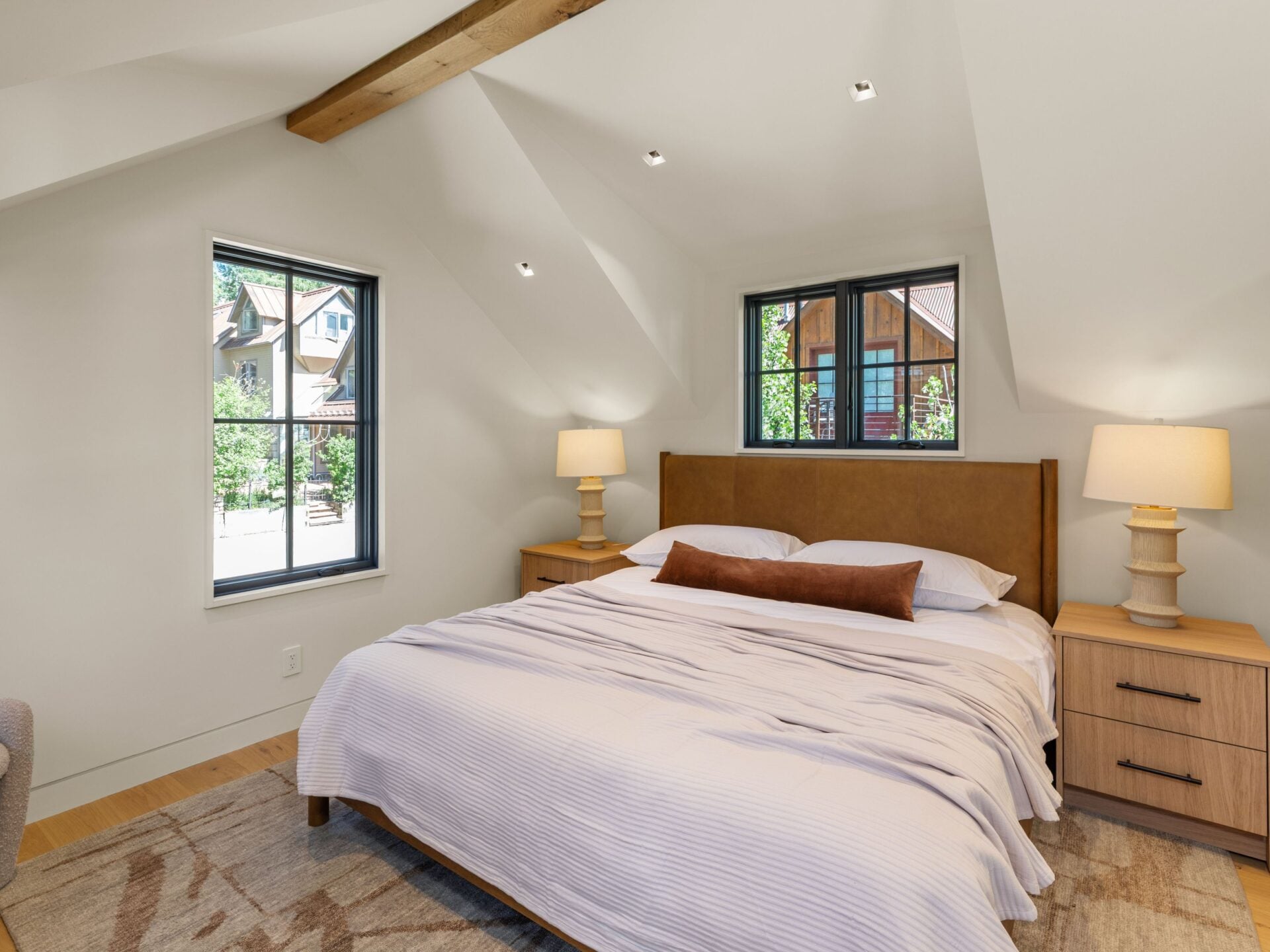 Black-framed windows bring in light from two sides, while warm wood nightstands and a leather-upholstered bed create the perfect separate space for guests.