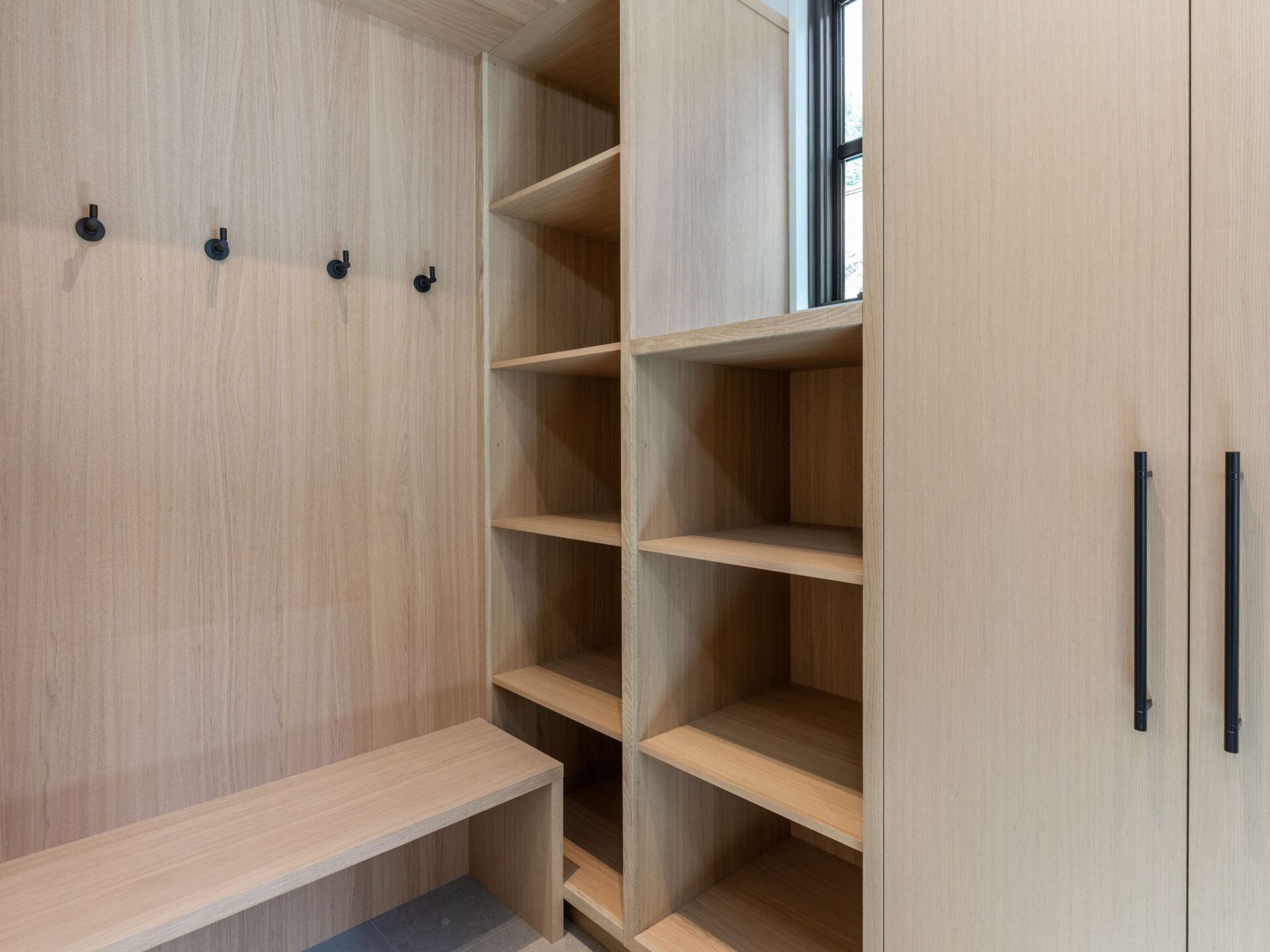 Ski room with built-in shelving, tall storage cabinets, wall hooks, and a long bench.