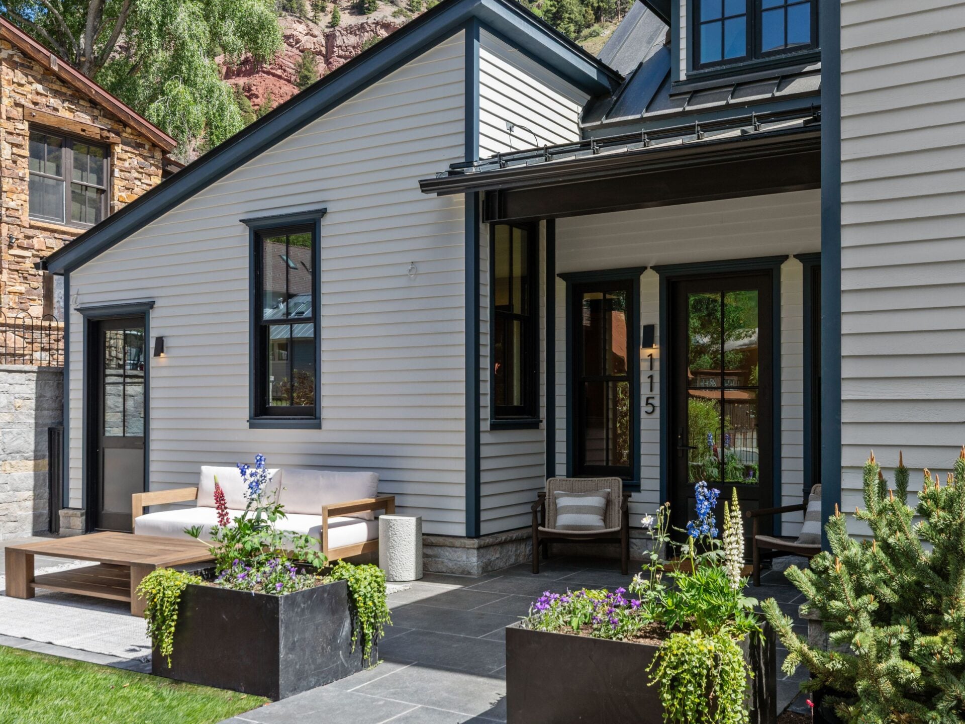 From there, the path leads to a front patio tucked beside the roofline, where a small seating area sits beside the entrance. 