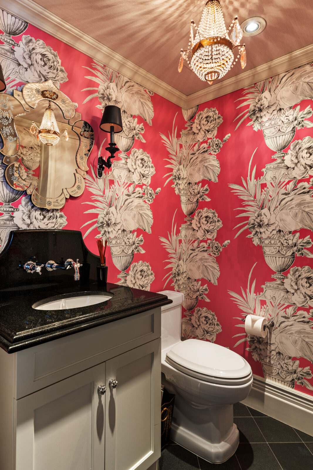 Above the vanity, a sculptural mirror reflects the room's crystal light fixture, while the dark tile floor keeps the lower half visually grounded against the more vivid colors.