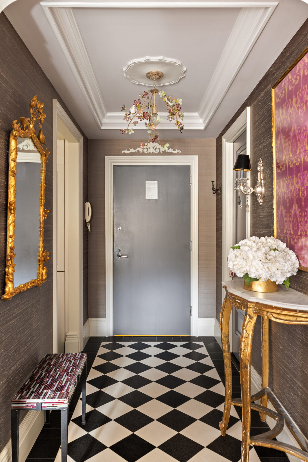 The entry foyer opens to the layered interiors curated by Heidi James of Studio LXIV, starting with checkerboard flooring and textured Elizabeth Dow wallpaper wrapping the walls.