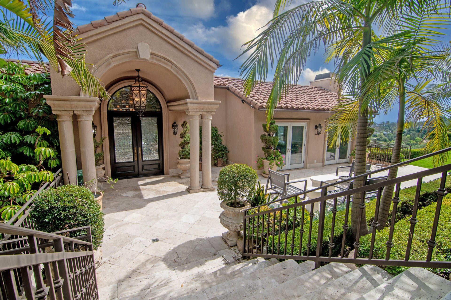 Gates open to a descending set of stairs that leads into a landscaped front courtyard and lawn before reaching the main entrance.