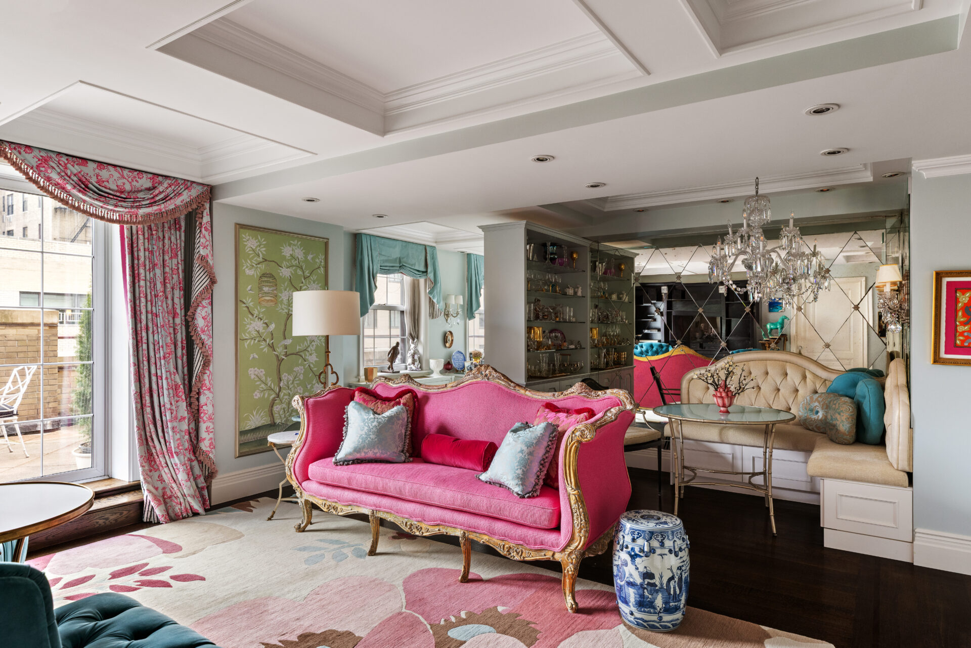 The living room where custom millwork wraps the space and a built-in banquette is tucked in the corner behind a pink couch and beneath a mirrored wall. 