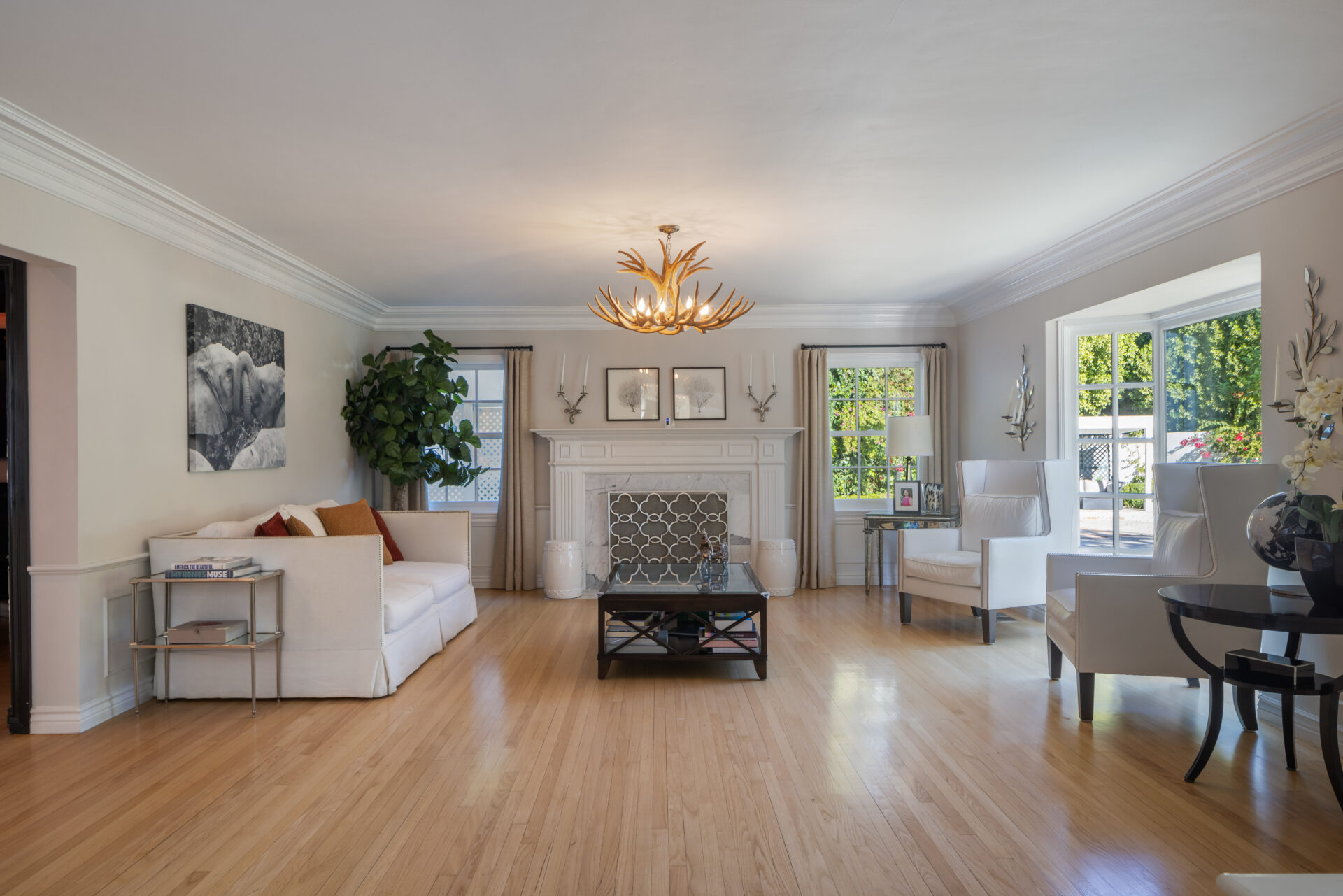 The checkered floor turns into hardwood as you enter the living room, where an antler chandelier hangs over a white fireplace framed by windows on either side. 
