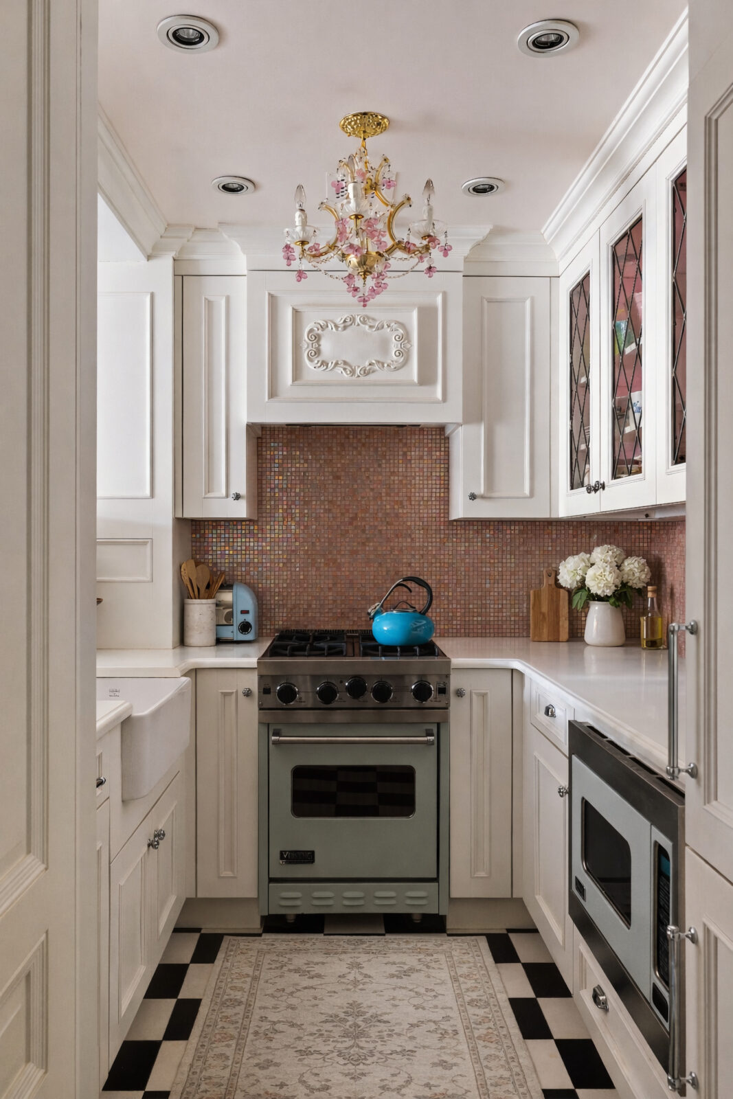The checkerboard flooring continues into the kitchen, where white cabinetry wraps the narrow space around a powder-blue Viking range and ceramic farmhouse sink. 