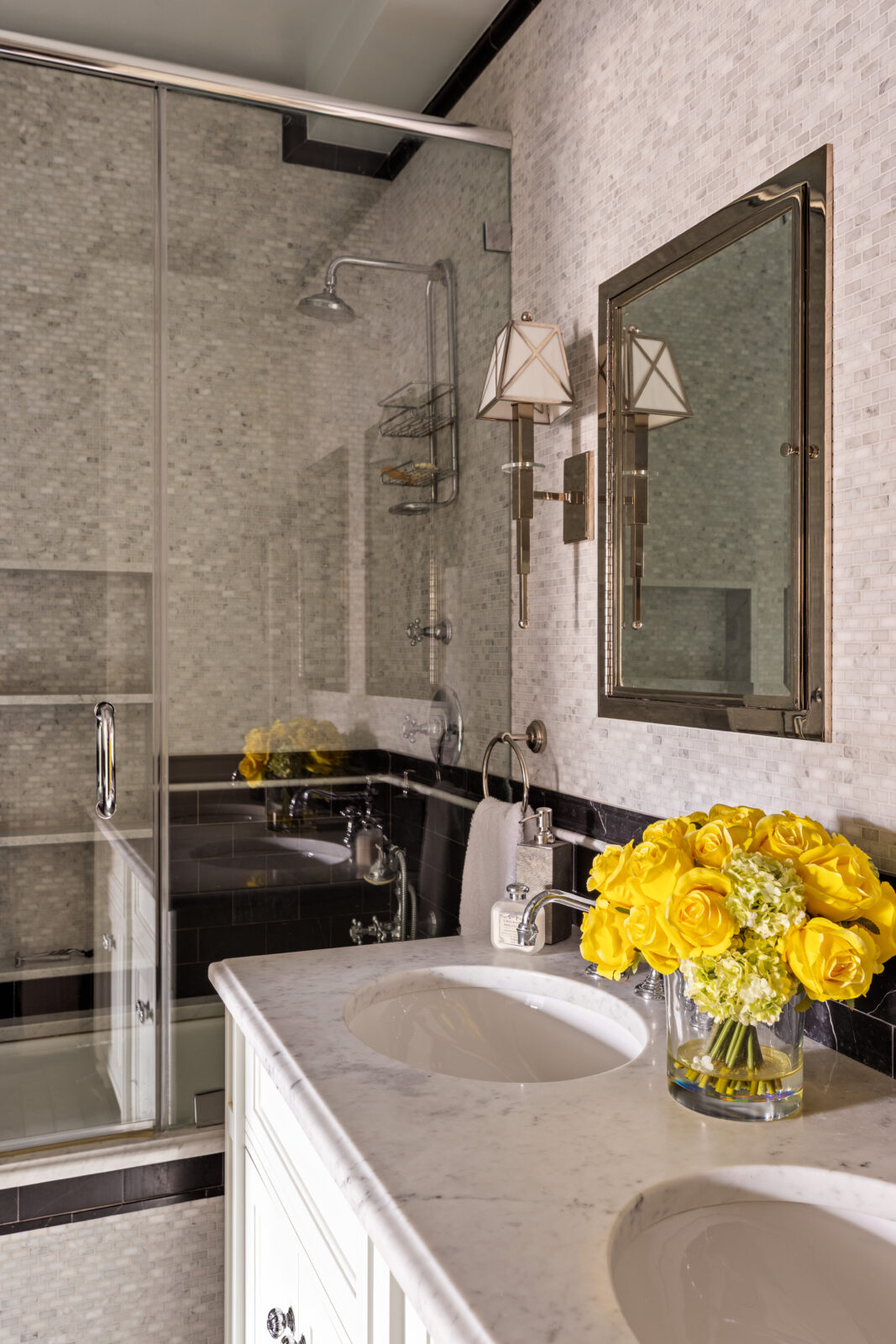 The renovated marble bathroom begins with a double vanity set beneath separate mirrors, with small-format marble tile extending across the walls. 